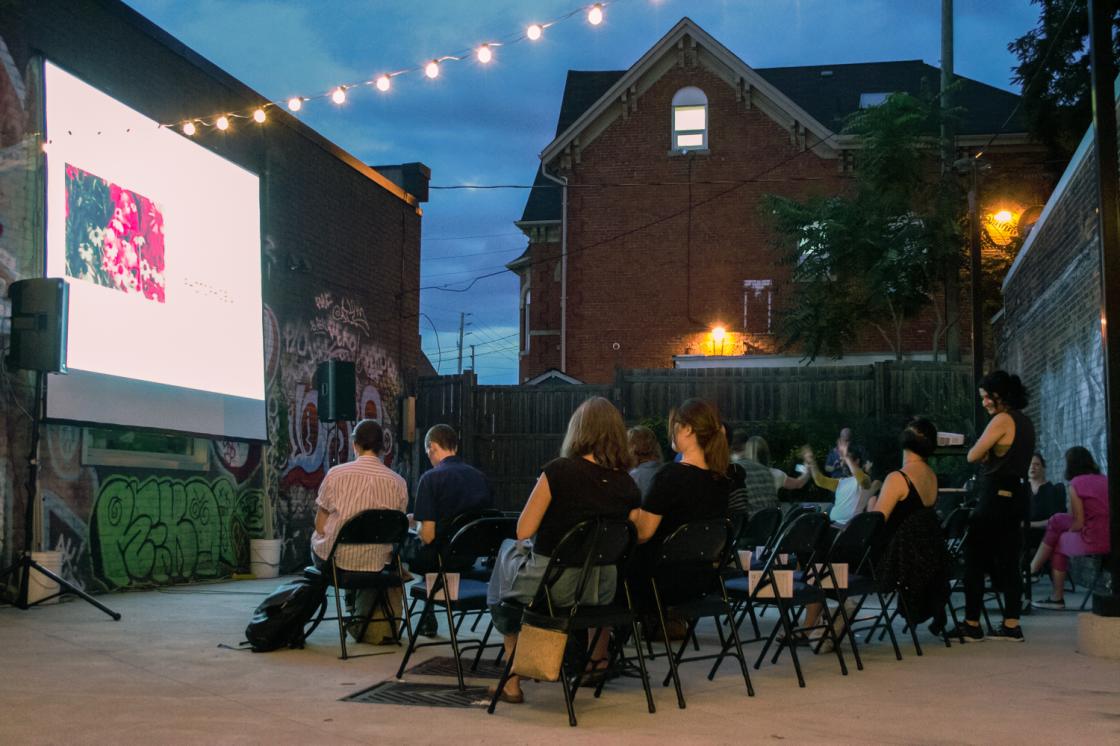People sitting and watching a film projected onto a wall outside