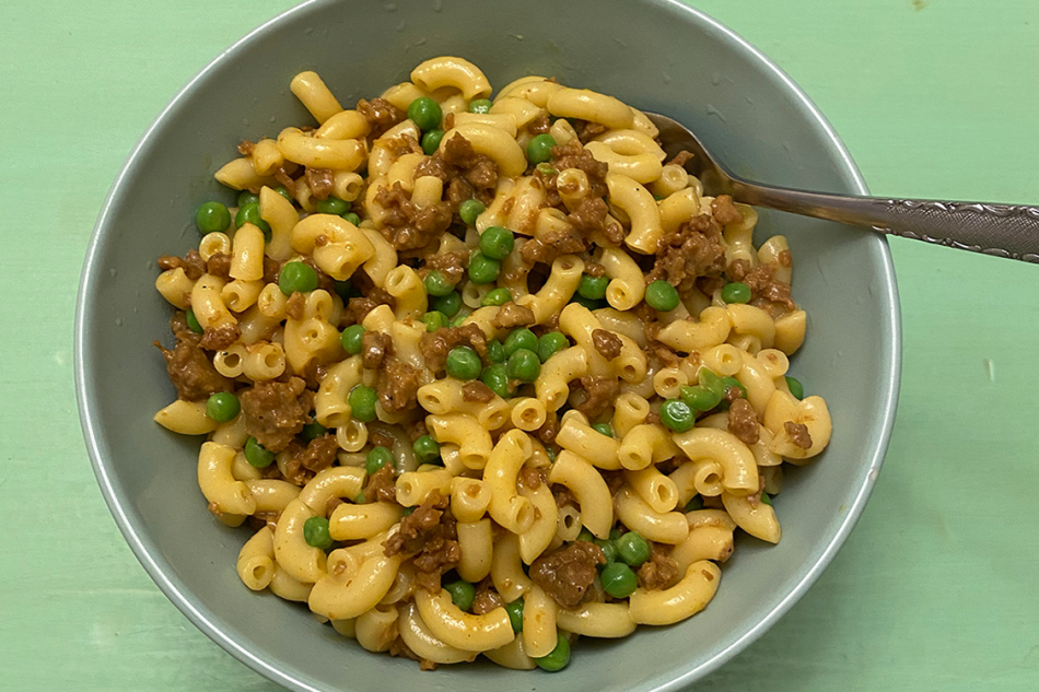 image of a bowl of mac and cheese with ground beef and peas on a bright mint green table