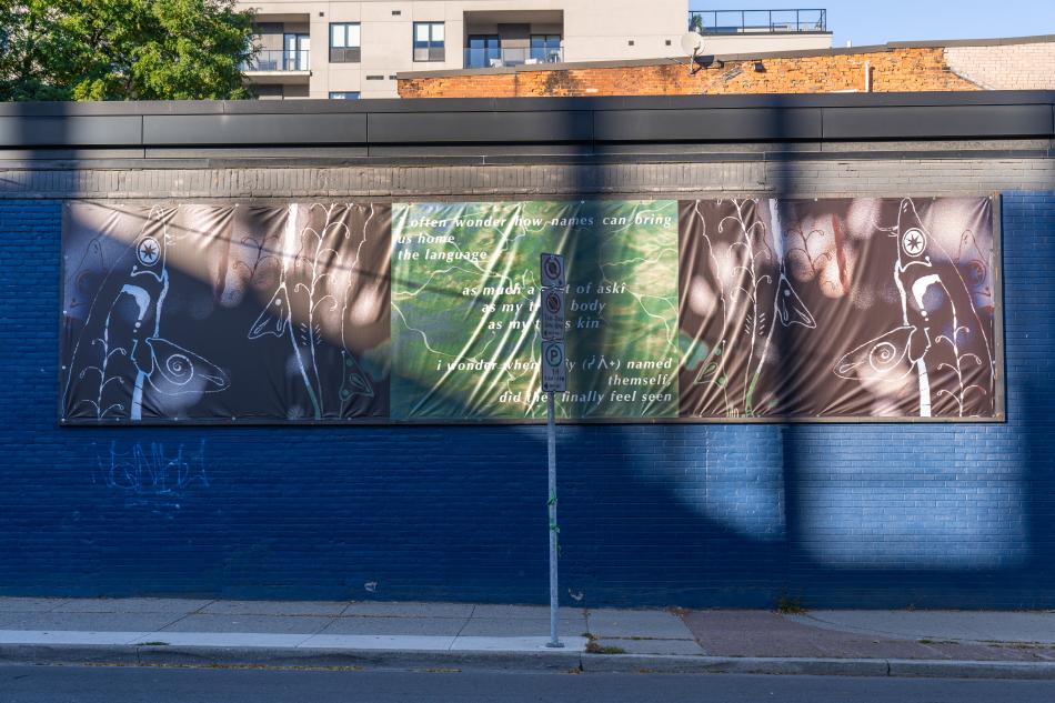 A photo of a billboard on our Cannon Street wall, the brick behind the billboard is dark blue, and there is a shadow being cast over the billboard. The billboard is by Theo Donovan - "I wonder when sîpîy (ᓰᐲᕀ) named themself, did they finally feel seen" is a mixed media photographic collage billboard that uses a combination of physical drawing, digital manipulation and photography to tell the story of queer connections to the land. A fractal pattern dances across the water."